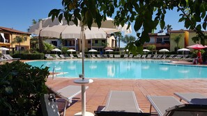 A swimming pool with lounge chairs and umbrellas, surrounded by buildings with balconies.