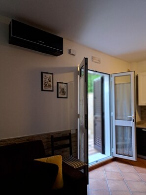 An open sliding door leading to a kitchen area, a wall-mounted air conditioner, and two framed pictures on the wall.