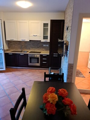 A kitchen with white cabinets, a microwave, and a stove. There is a dining table with chairs and a vase of flowers.