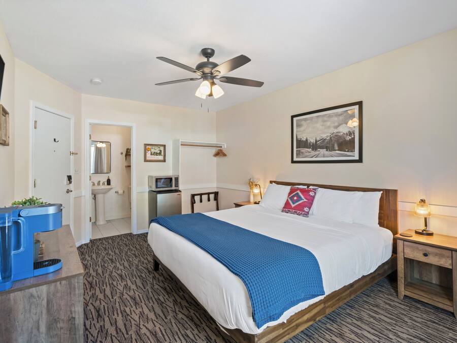 A hotel room with a bed, a desk, a coffee maker, a nightstand, and a ceiling fan.