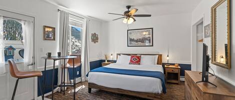 A bedroom with a bed, a desk, a chair, a ceiling fan, and a large mirror.