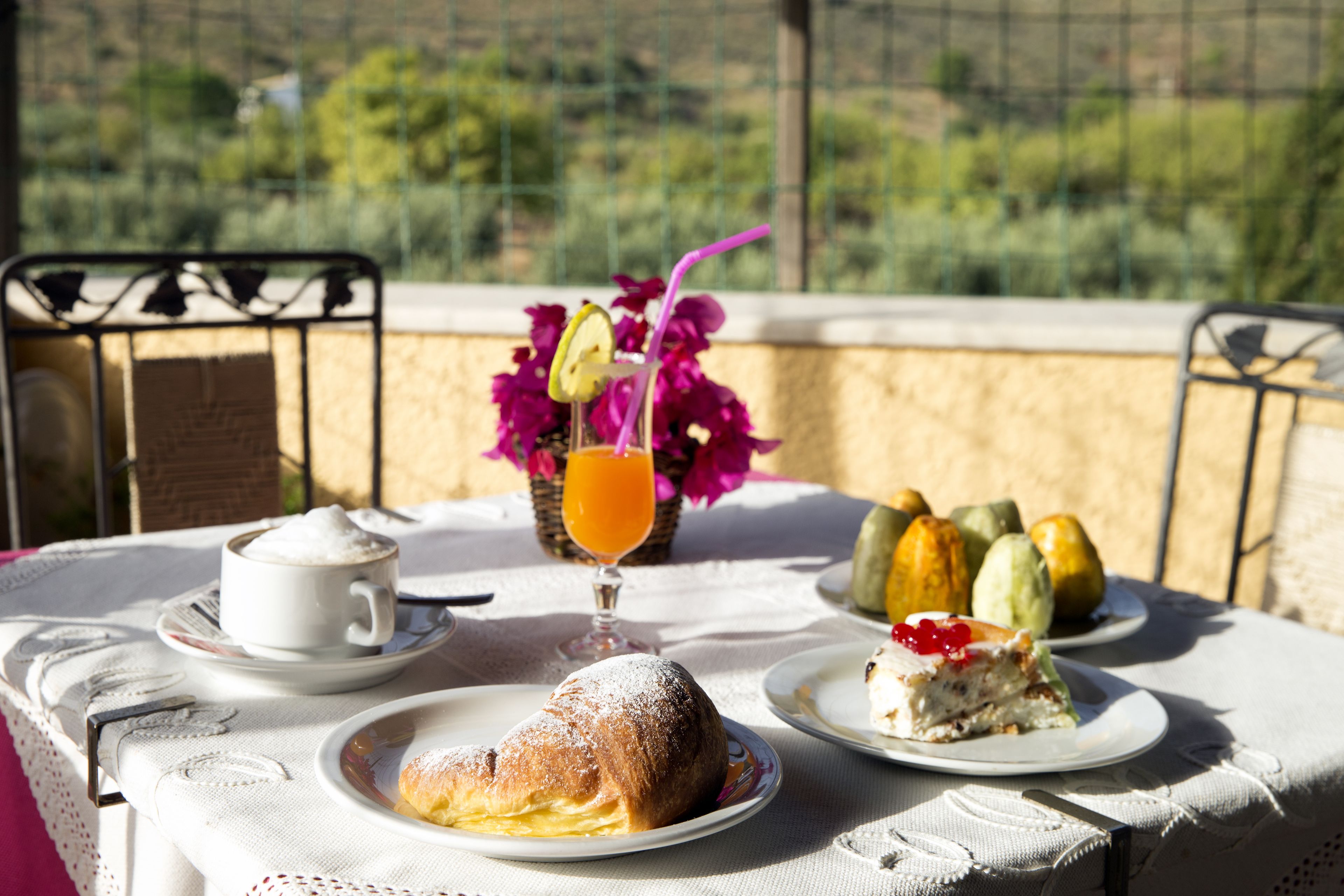 A table with a white tablecloth, a cup of coffee, a glass of orange juice, a pastry, and a plate with a slice of cake.