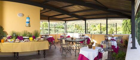 An outdoor patio with tables and chairs, a covered area, and a view of a hilly landscape.