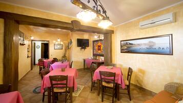Un espace repas avec des tables recouvertes de nappes roses, des chaises en bois et un lustre.