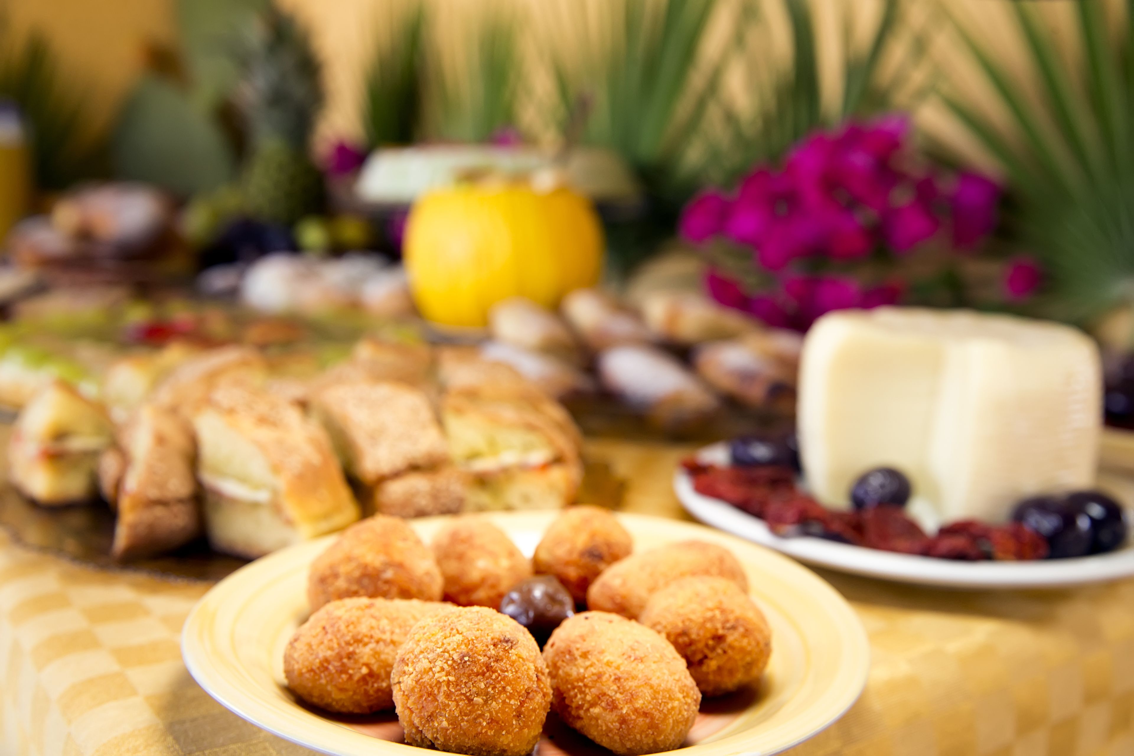 Una mesa con diversos alimentos, como croquetas, un queso rueda y frutas.