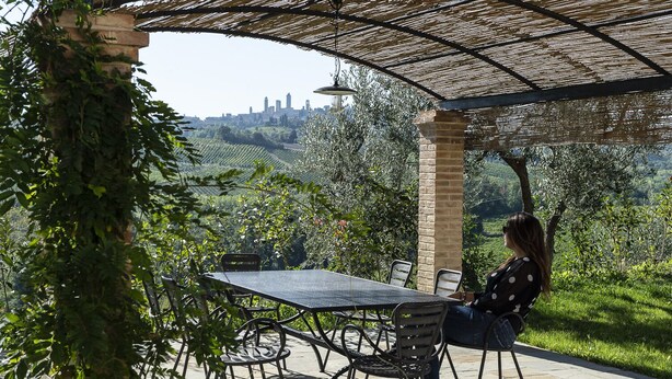 An outdoor patio with a table and chairs, surrounded by greenery and a cityscape view. - Gina, apartment overlooking the hills of San Gimignano (San Gimignano)