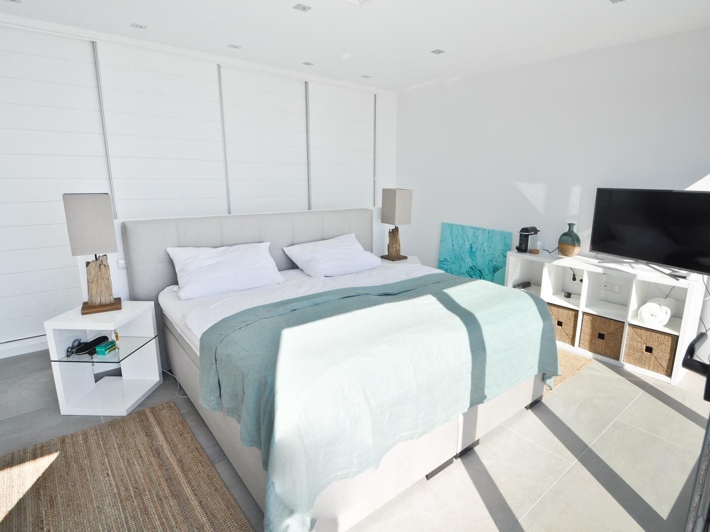 A modern bedroom with a large bed, bedside tables, a TV, and storage units.