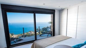 Une chambre dotée d’une grande porte-fenêtre coulissante donnant sur un balcon avec vue sur la mer et la ville.