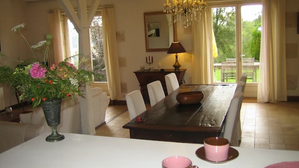 Uma sala de jantar com mesa de madeira, cadeiras, um lustre e vista para o exterior.