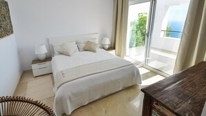 Ein Schlafzimmer mit Bett, Nachttischen, einem Sessel und Blick auf einen Balkon.