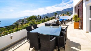 Eine Terrasse mit Glastisch und Korbstühlen, mit Blick auf eine malerische Seelandschaft und Berge.