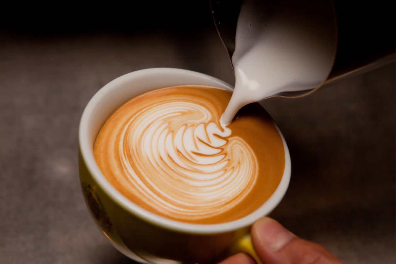 A hand holding a cup of coffee with latte art.