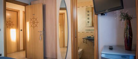 A hotel room with a bed, a TV, a mirror, and a bathroom visible through an open door.