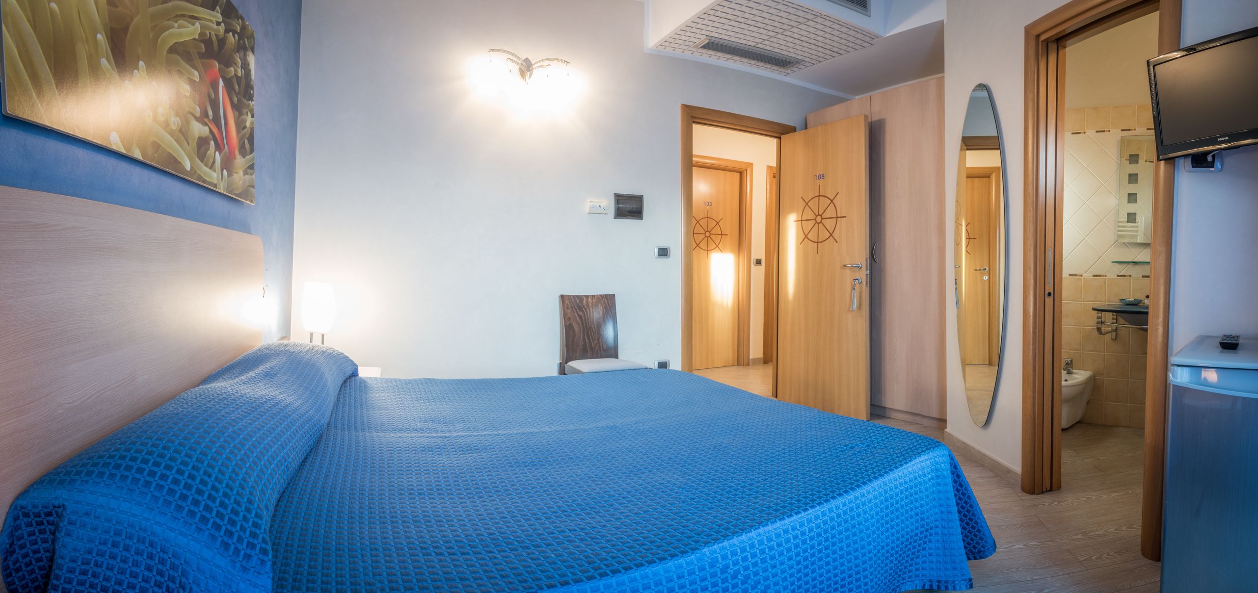 Una camera d'albergo con un letto, un armadio, uno specchio e una televisione.