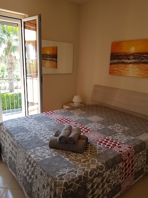 Un dormitorio con una colcha estampada, vistas al exterior a través de una puerta corrediza y dos cuadros en la pared.