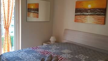 Una camera da letto con una coperta a motivi, un letto rifatto con asciugamani arrotolati, un comodino con una lampada e due quadri alle pareti.