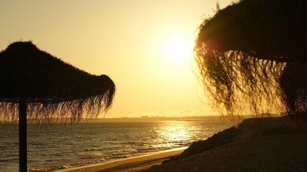 A beach scene with a thatched umbrella and a rocky shoreline. - Villa Vista Mar (Loulé)