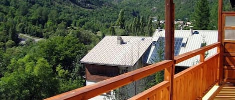 A wooden balcony with a view of a mountainous landscape and a building with solar panels.