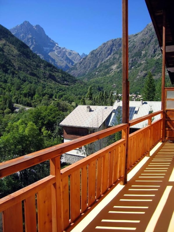 A wooden balcony with a view of a mountainous landscape and a building with solar panels.