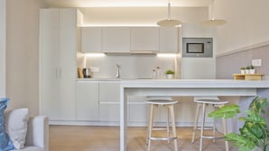 Une cuisine moderne avec des meubles blancs, un îlot central doté de tabourets, un éclairage suspendu et un four à micro-ondes.