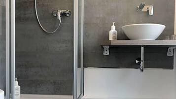 Ein modernes Badezimmer mit einer Duschkabine aus Glas, einem weißen Waschbecken und einem dunklen Holzboden.