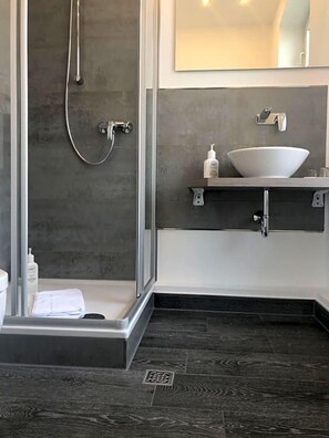 A modern bathroom with a glass shower enclosure, a white sink, and a dark wood floor.