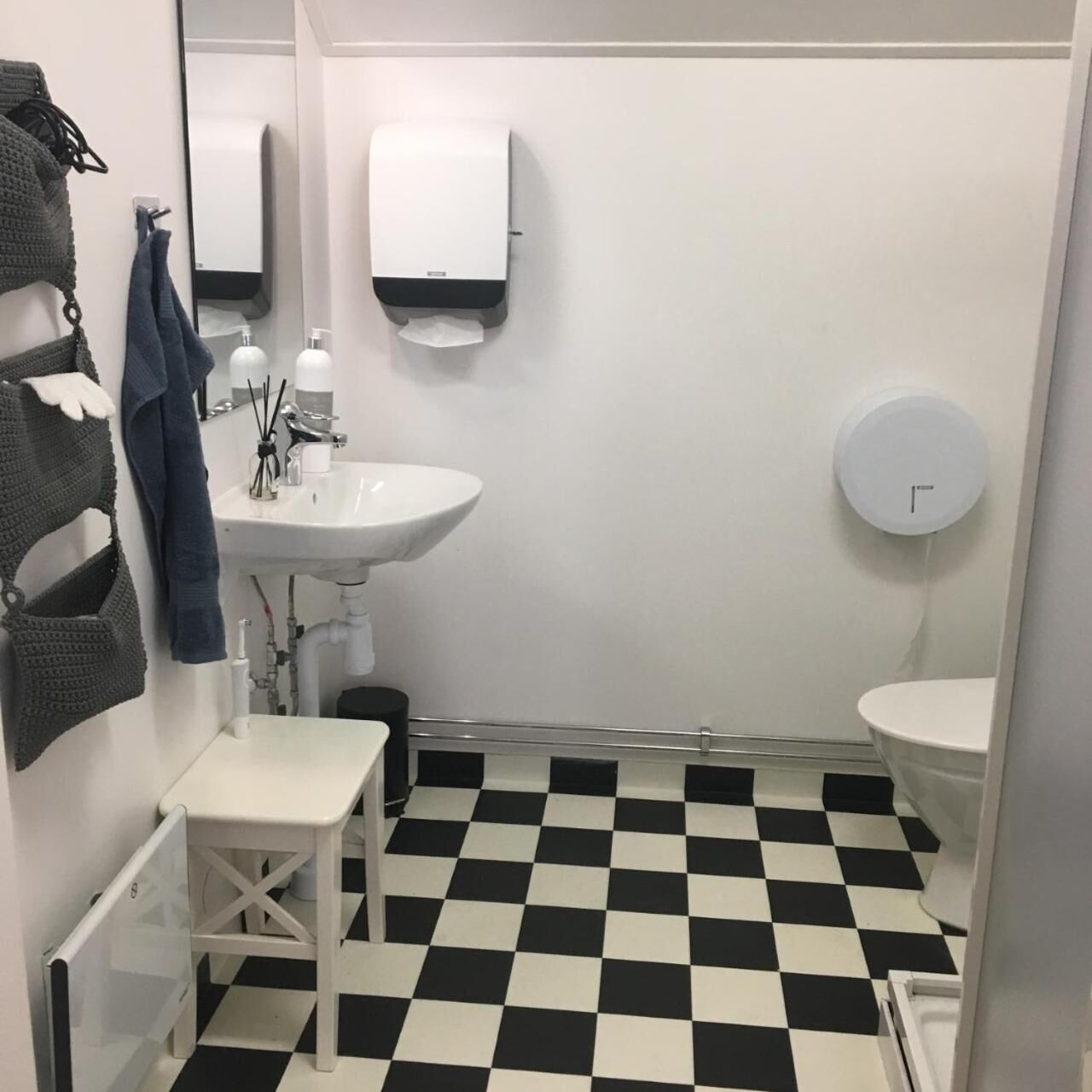 A bathroom with a white sink, a toilet, a black and white checkered floor, a towel rack, and a soap dispenser.