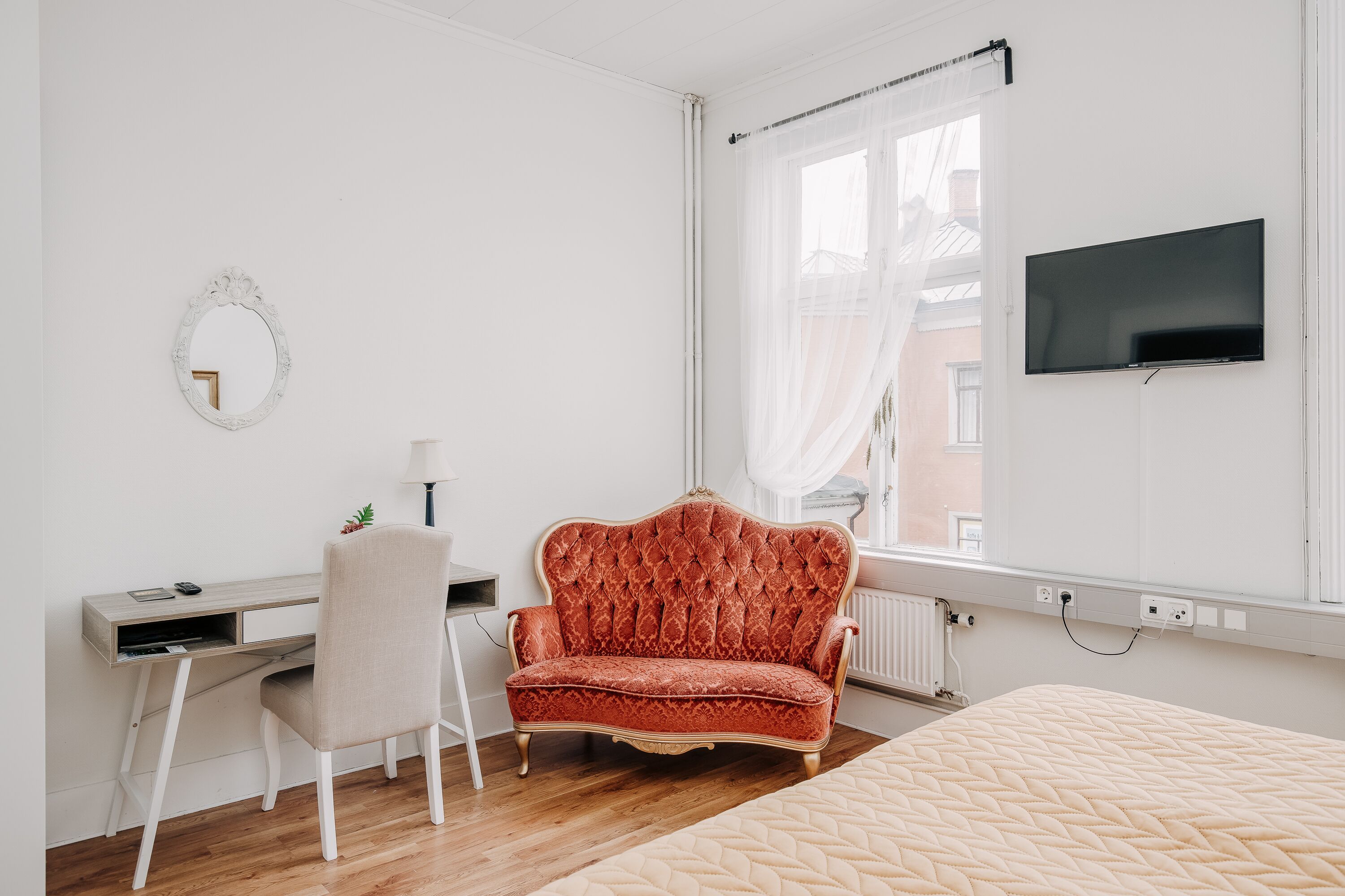 A bedroom with a bed, a desk, a chair, a TV, and a window with curtains.