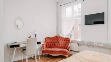 A bedroom with a bed, a desk, a chair, a TV, and a window with curtains.