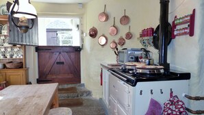 Een keuken met een fornuis, pannen, een magnetron en een houten tafel.