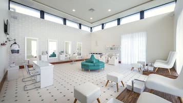 A modern hotel room with a large mirror, a teal sofa, white armchairs, and a reception desk.