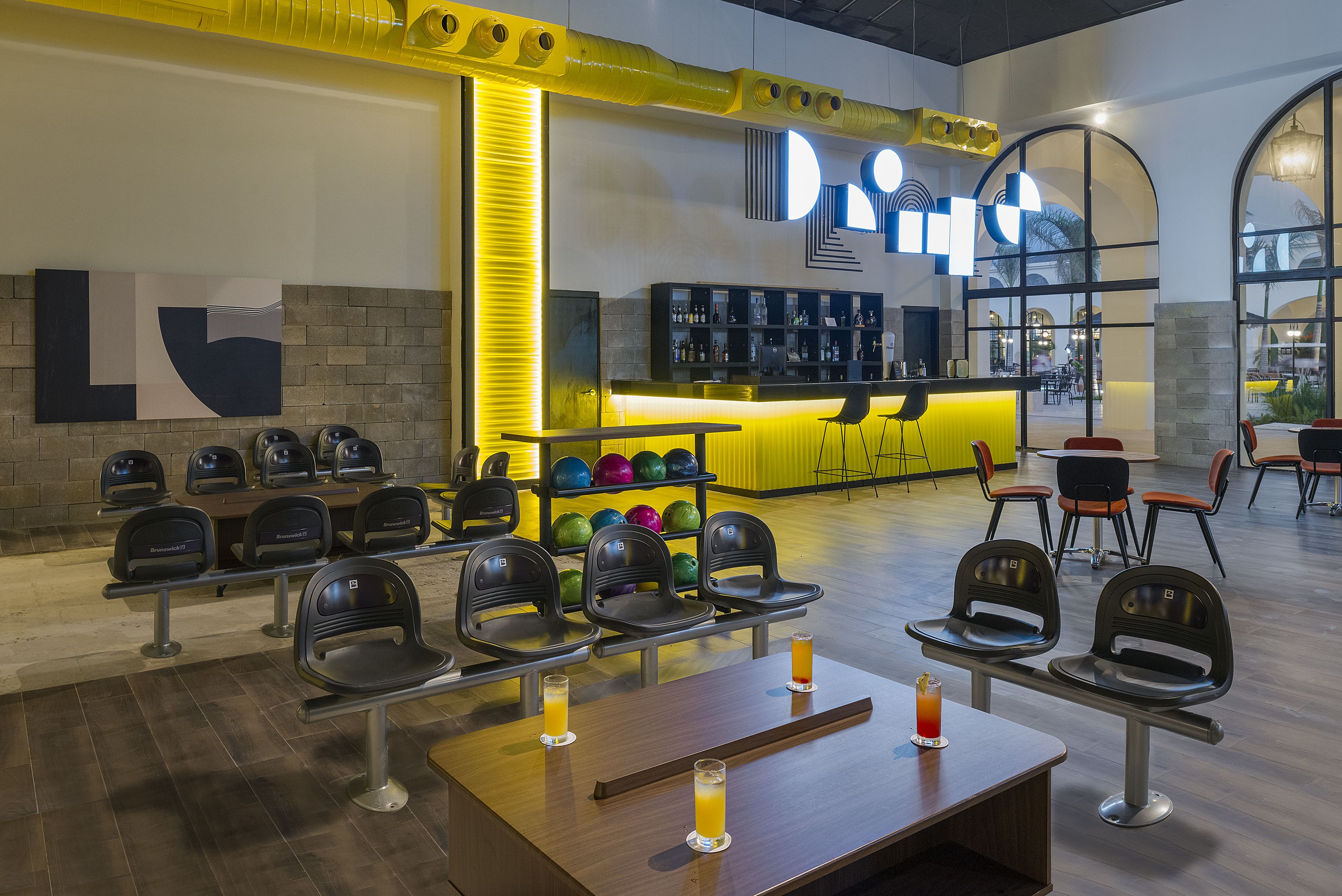 A bowling alley with multiple lanes, seating areas, and a bar with a neon sign.