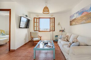 A living room with a sofa, a coffee table, a chair, a television, and a window with open shutters. - Caleta de Fuste Relax (CALETA DE FUSTE)