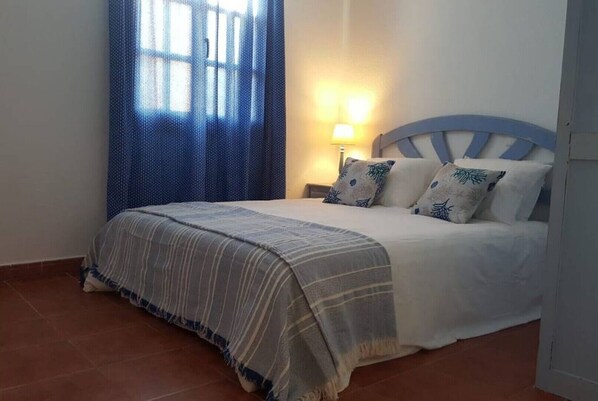 Una camera da letto con un letto, un comodino, una lampada e una finestra con tende.