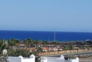 A coastal view with a clear sky, palm trees, and a road leading to a beach. - Caleta de Fuste Relax (CALETA DE FUSTE)