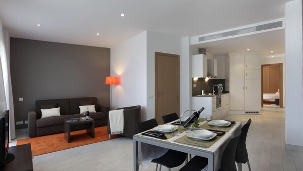 A modern living room with a sofa, coffee table, and dining area with chairs and a table set for two.