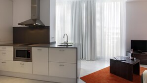 Una cocina moderna con horno empotrado, campana extractora de acero inoxidable y un amplio ventanal con cortinas traslúcidas.