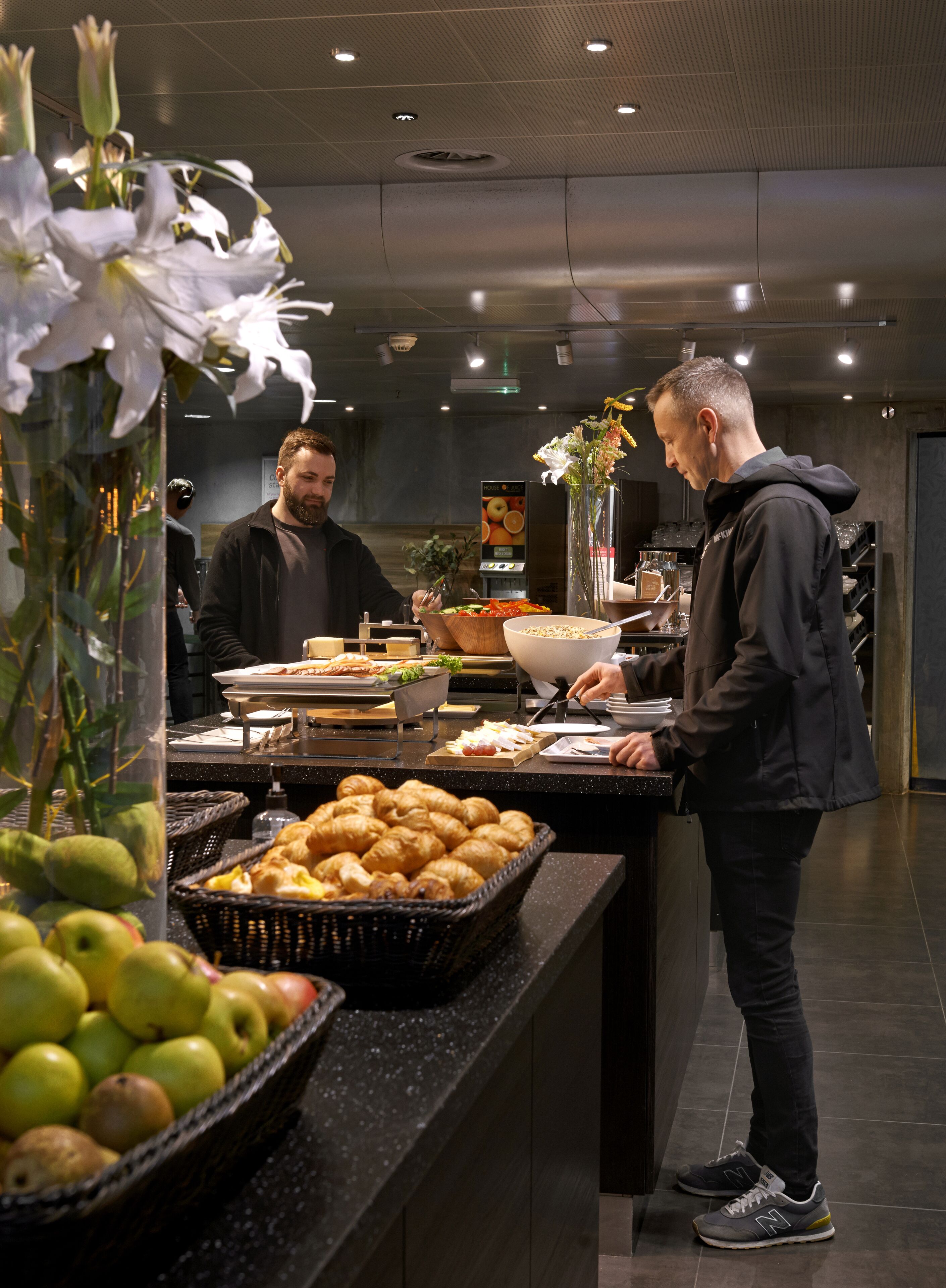 A buffet area with various food items, including fruits and pastries, and a man serving himself.