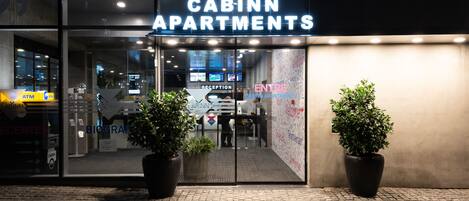 Exterior de Cabinn Apartments, con recepción, cajeros automáticos y plantas en macetas.