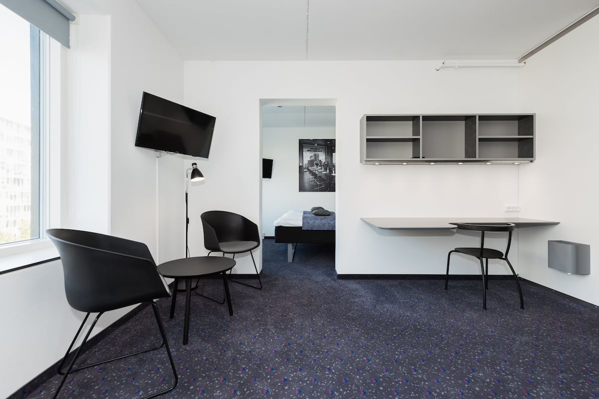 Une chambre d’hôtel moderne dotée d’une grande fenêtre, d’un téléviseur à écran plat, d’un bureau avec une chaise et d’un lit.
