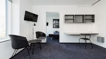 A modern hotel room with a flat-screen TV, a desk with a chair, a small table, and a sofa.