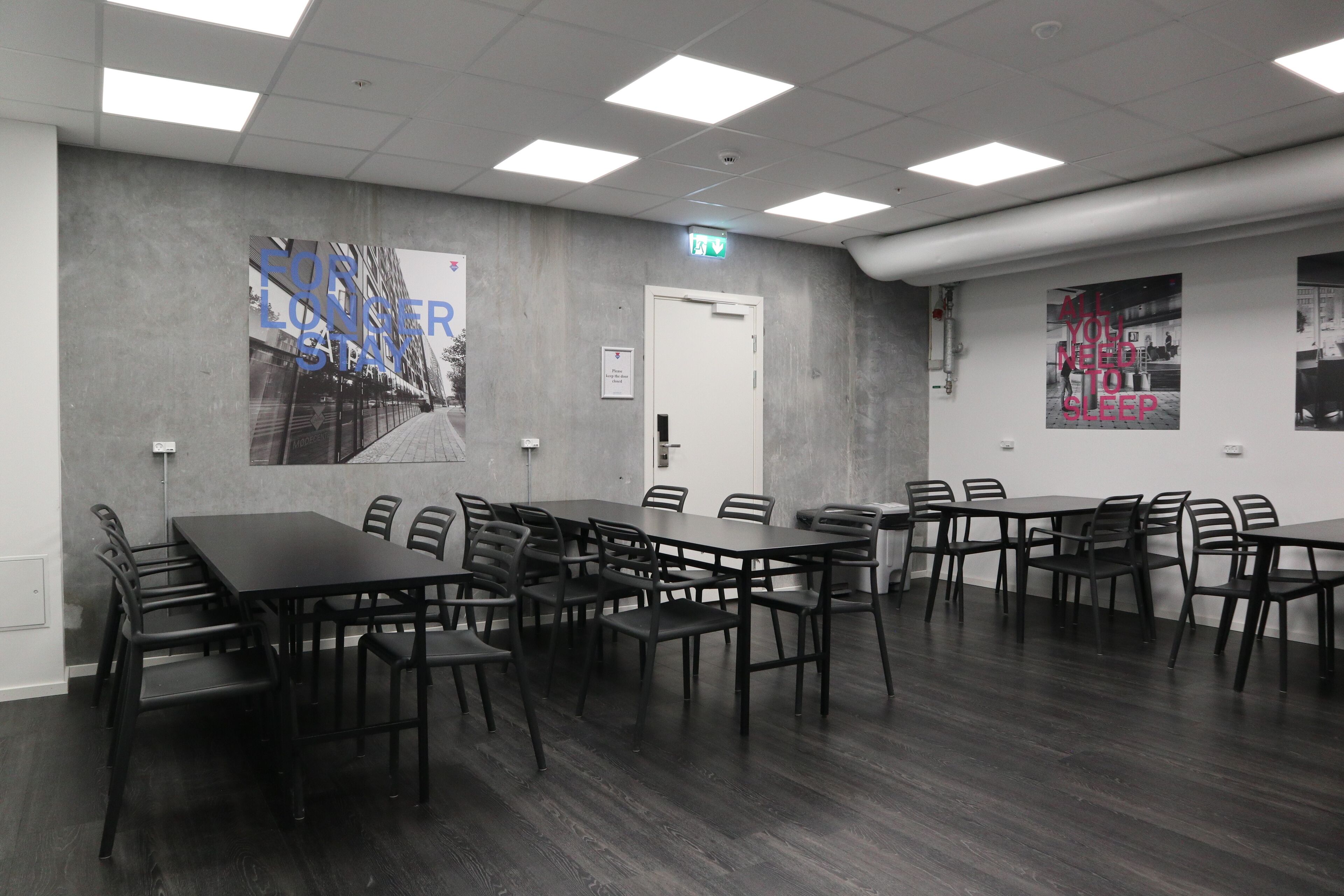 A conference room with multiple tables and chairs, a door, and two posters on the walls.