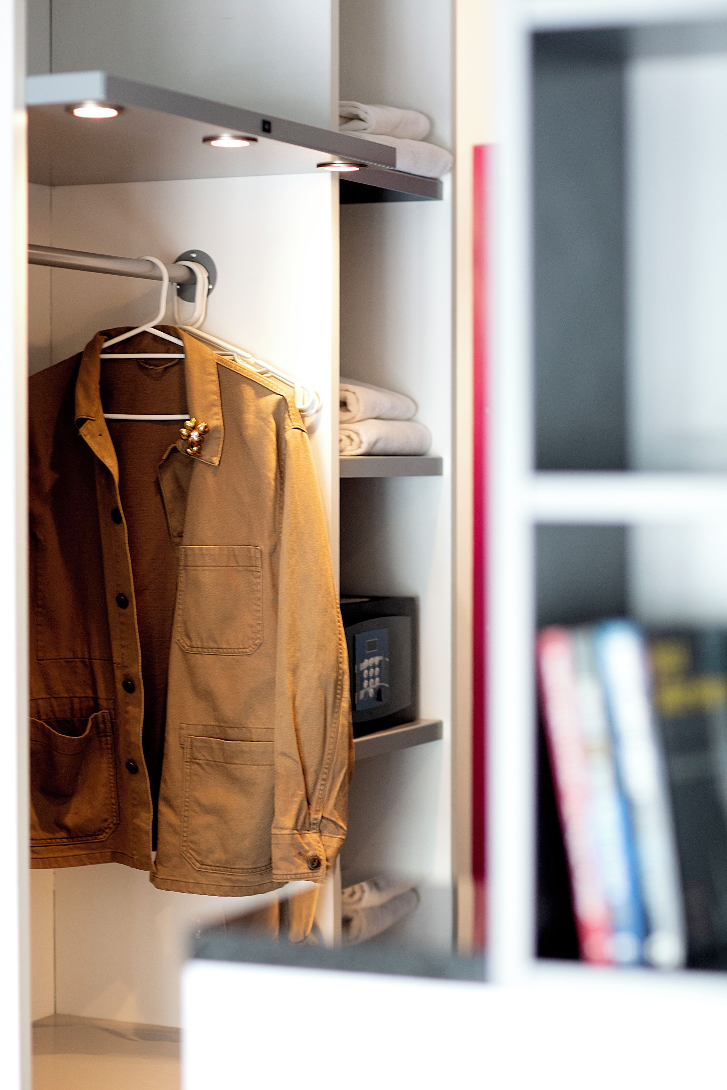 Een kast met een kledingroede en planken met opgevouwen kleding en een klein apparaat.