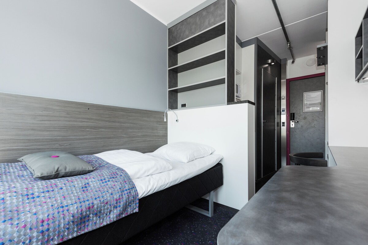 A modern bedroom with a bed, built-in shelving, a desk, and a door leading to a bathroom.