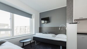 A modern hotel room with a bed, a small table, a TV mounted on the wall, and a minibar. - CABINN Apartments (Copenhagen)