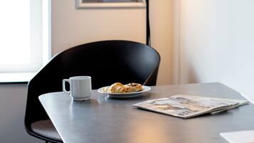 Ett modernt kontorsutrymme med ett skrivbord, en stol, en kaffekopp, en tallrik med croissanter, en lampa och inramade informationsaffischer på väggen.