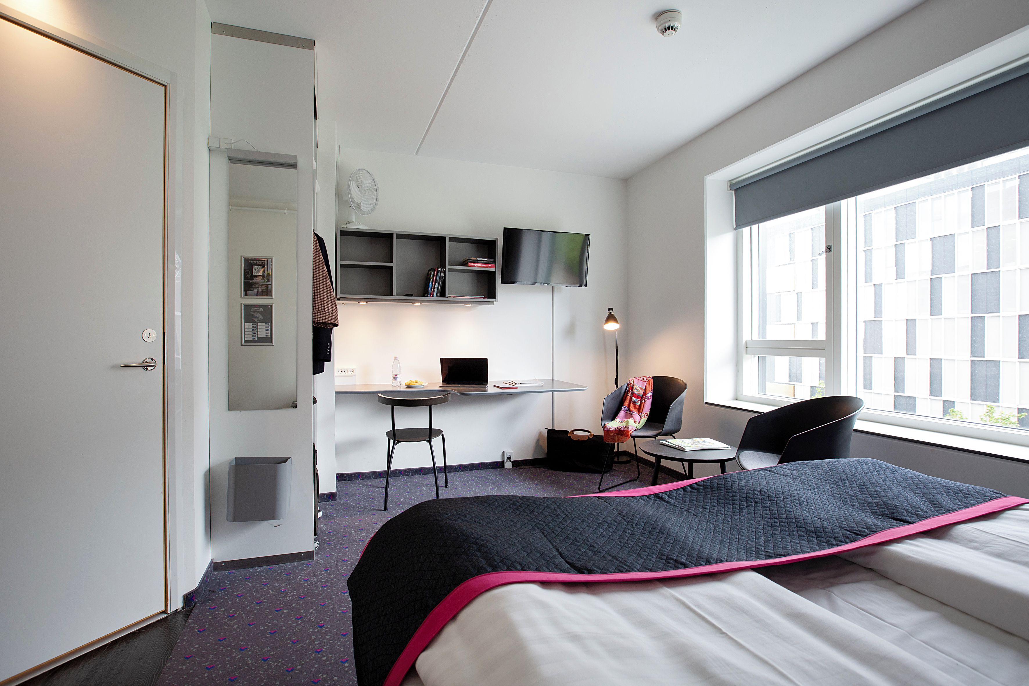 A hotel room with a bed, a desk, a chair, a TV, and a window.