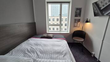 Een hotelkamer met een bed, een raam, een stoel en een tv aan de muur.
