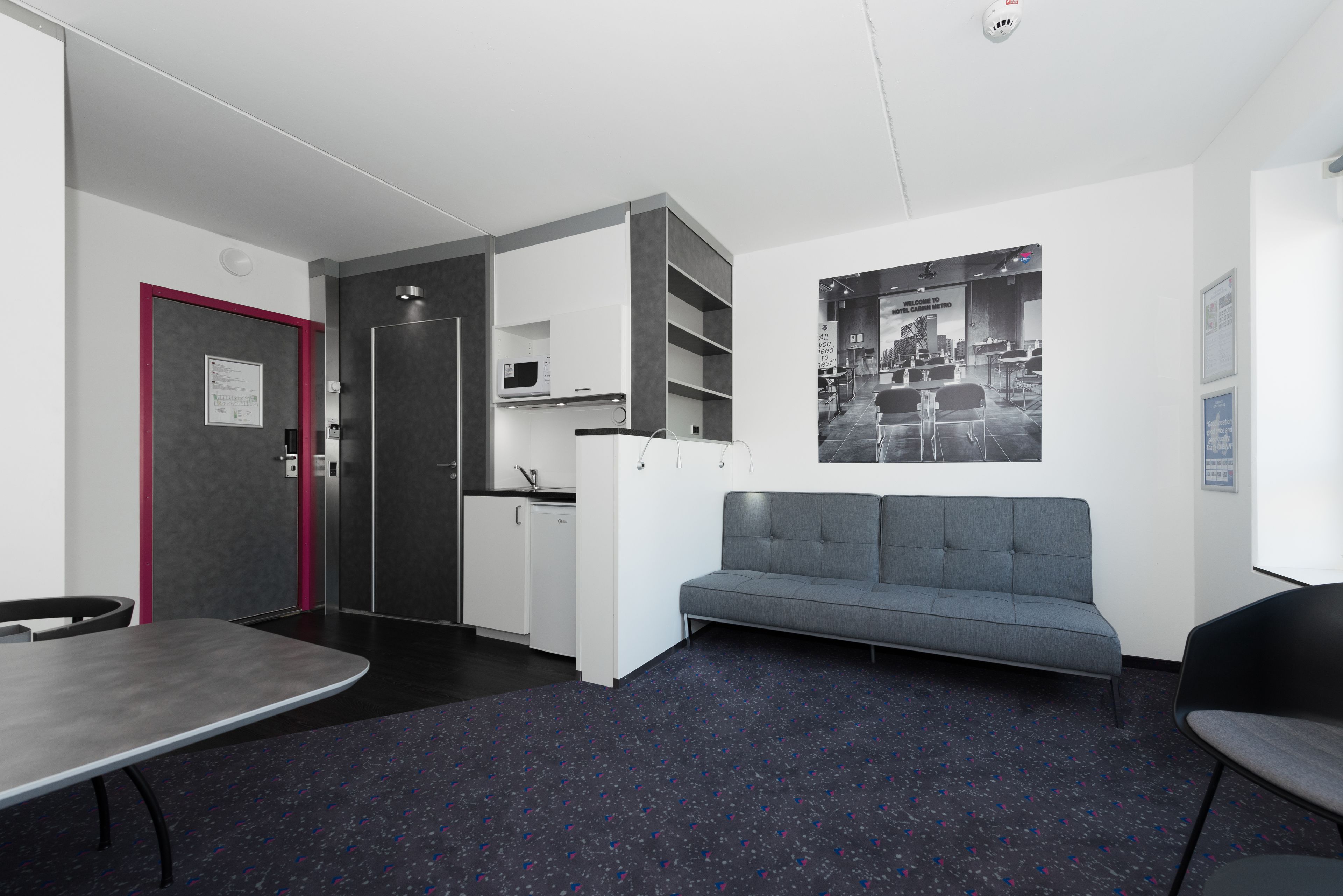 A modern office space with a kitchenette, a grey sofa, and a dining table.