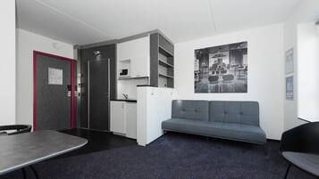 A modern office space with a kitchenette, a grey sofa, and a dining table.